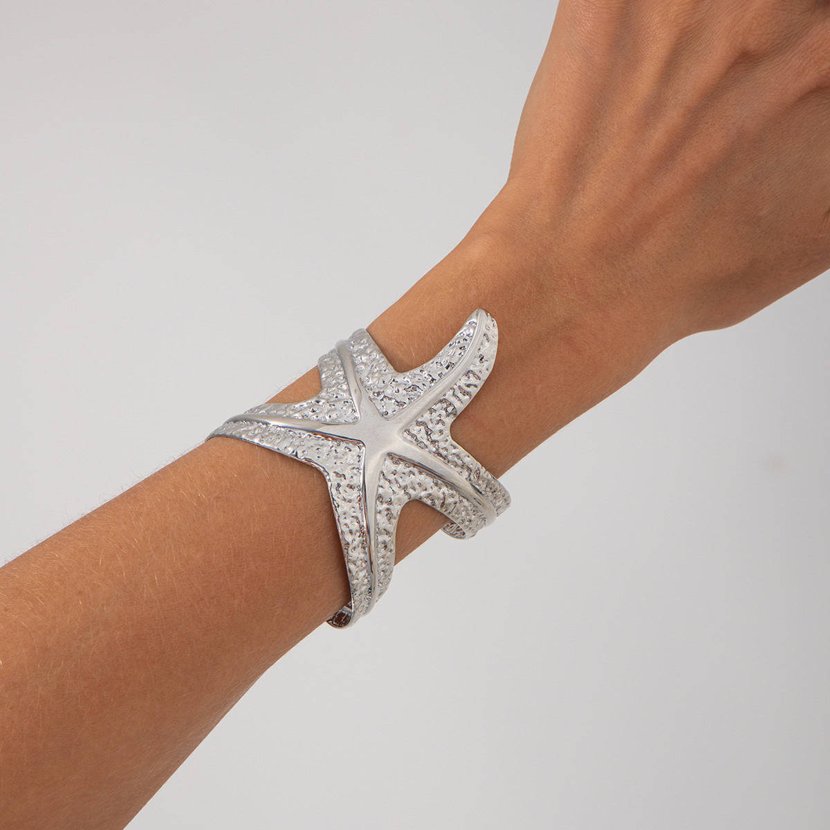Pulsera metálica con forma de estrella de mar exagerada y acabado galvanizado para un estilo playero y oceánico
