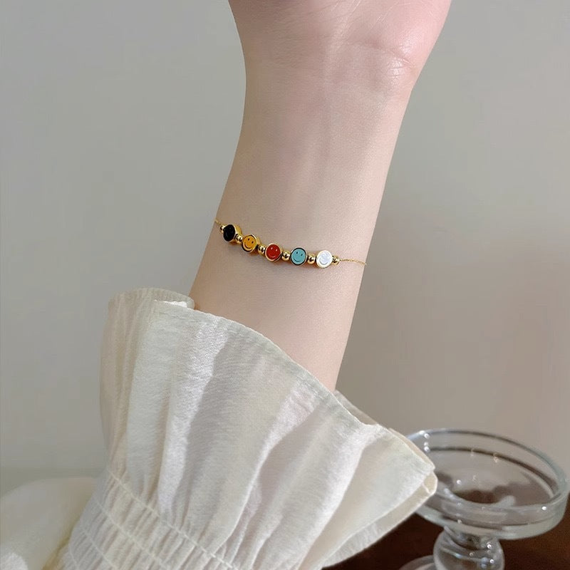 Bracciale da donna in acciaio al titanio con ciondolo sorridente minimalista, finitura smaltata e perline con accenti in oro 18 carati