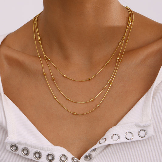 Collana da donna a più strati con perle dorate in acciaio inossidabile placcato e acciaio al titanio, con dettagli geometrici e linee delicate
