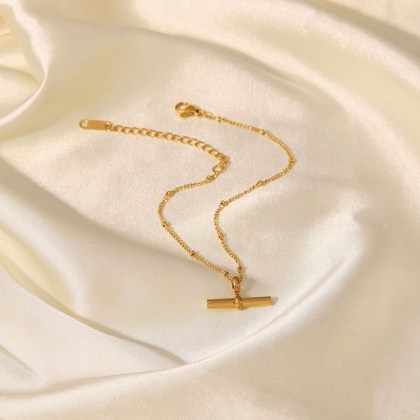 Tobillera minimalista geométrica de titanio y acero con colgante de barra en T chapado en oro de 18K y cadena de cuentas.