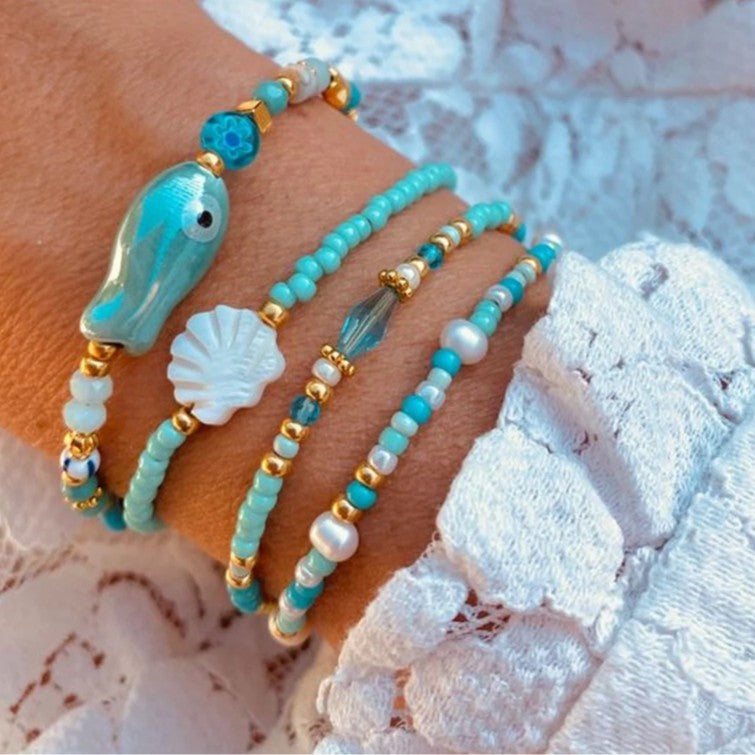Pulsera bohemia de vacaciones en la playa con abalorios de peces y conchas de cerámica en un hilo de cuentas multicapa