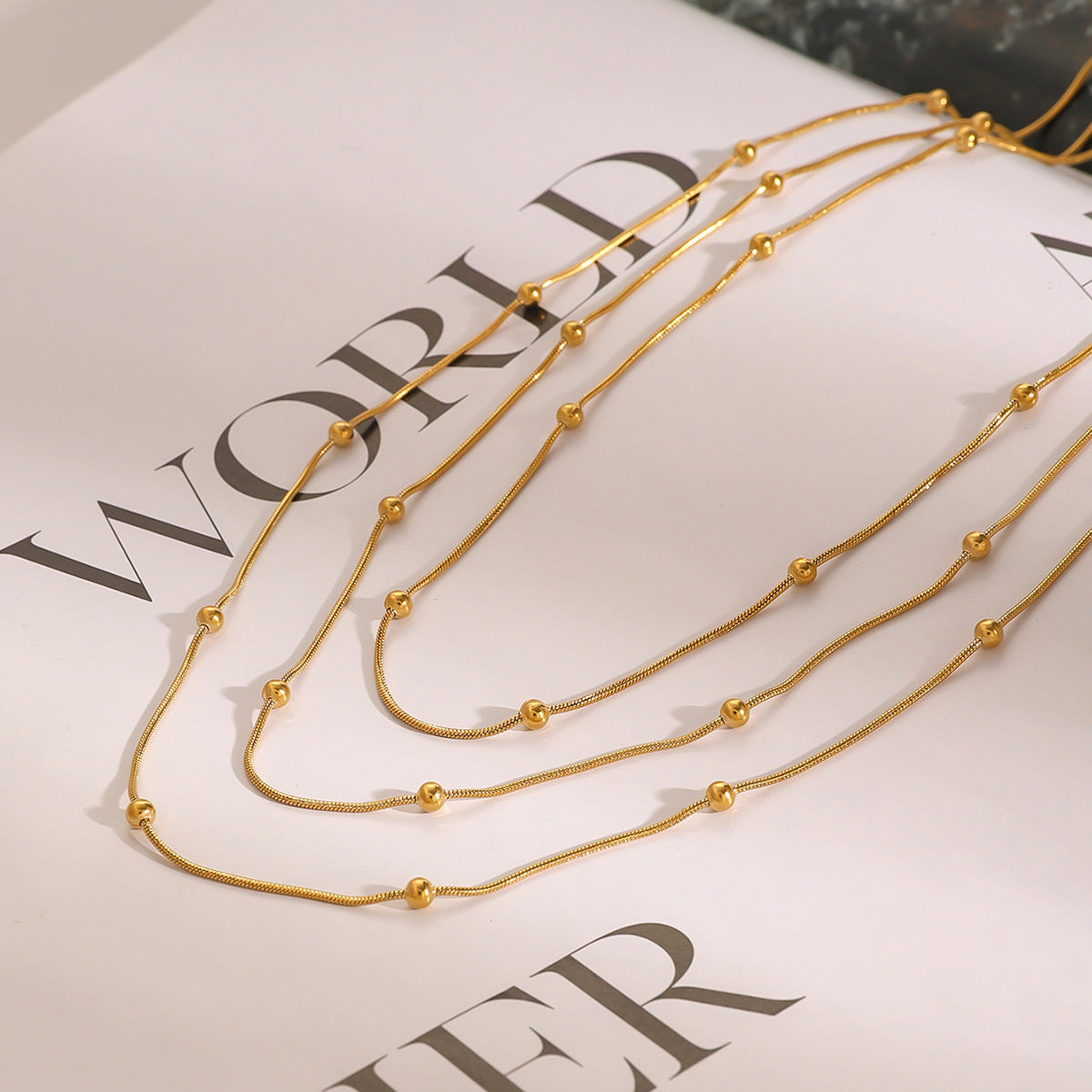 Collana da donna a più strati con perle dorate in acciaio inossidabile placcato e acciaio al titanio, con dettagli geometrici e linee delicate