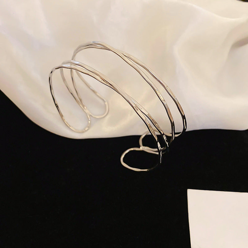 Bracciale rigido in metallo avvolto da linee geometriche irregolari, finitura placcata, stile minimalista, per un look da ufficio alla moda
