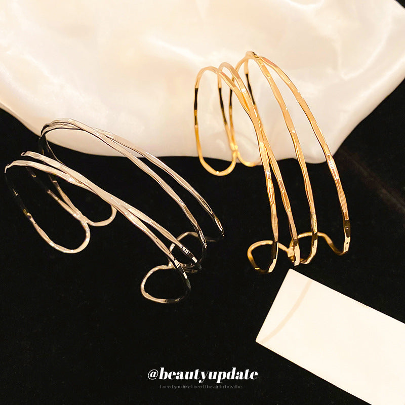 Bracciale rigido in metallo avvolto da linee geometriche irregolari, finitura placcata, stile minimalista, per un look da ufficio alla moda