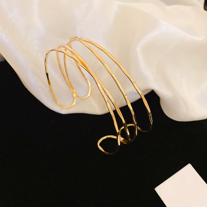 Bracciale rigido in metallo avvolto da linee geometriche irregolari, finitura placcata, stile minimalista, per un look da ufficio alla moda