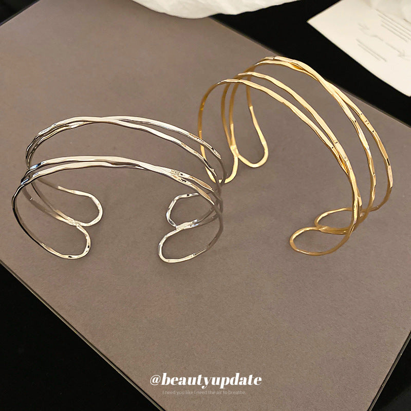 Bracciale rigido in metallo avvolto da linee geometriche irregolari, finitura placcata, stile minimalista, per un look da ufficio alla moda